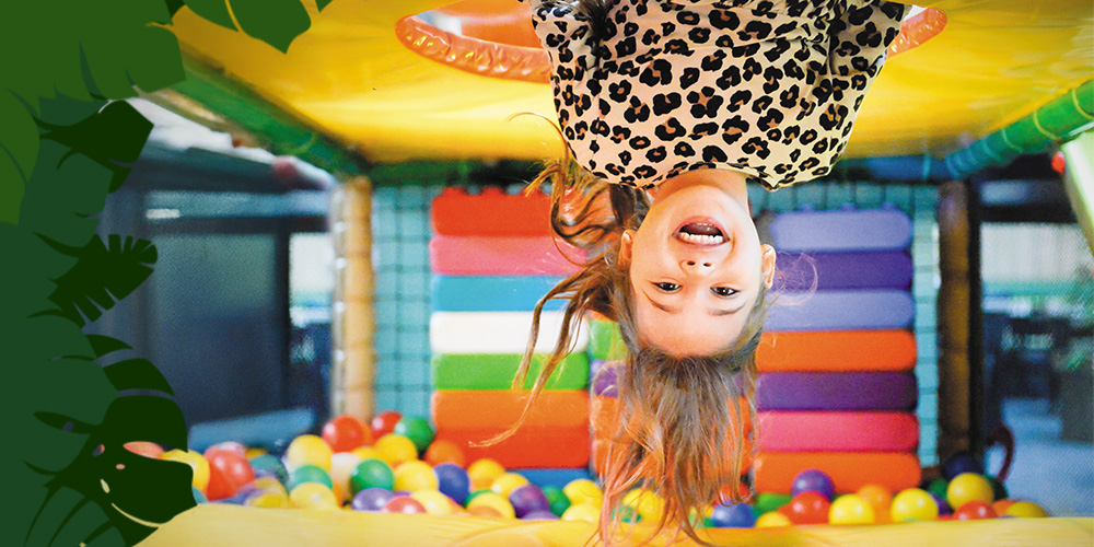 Meisje speelt lachend ondersteboven in het indoor speelparadijs van Monkey Town